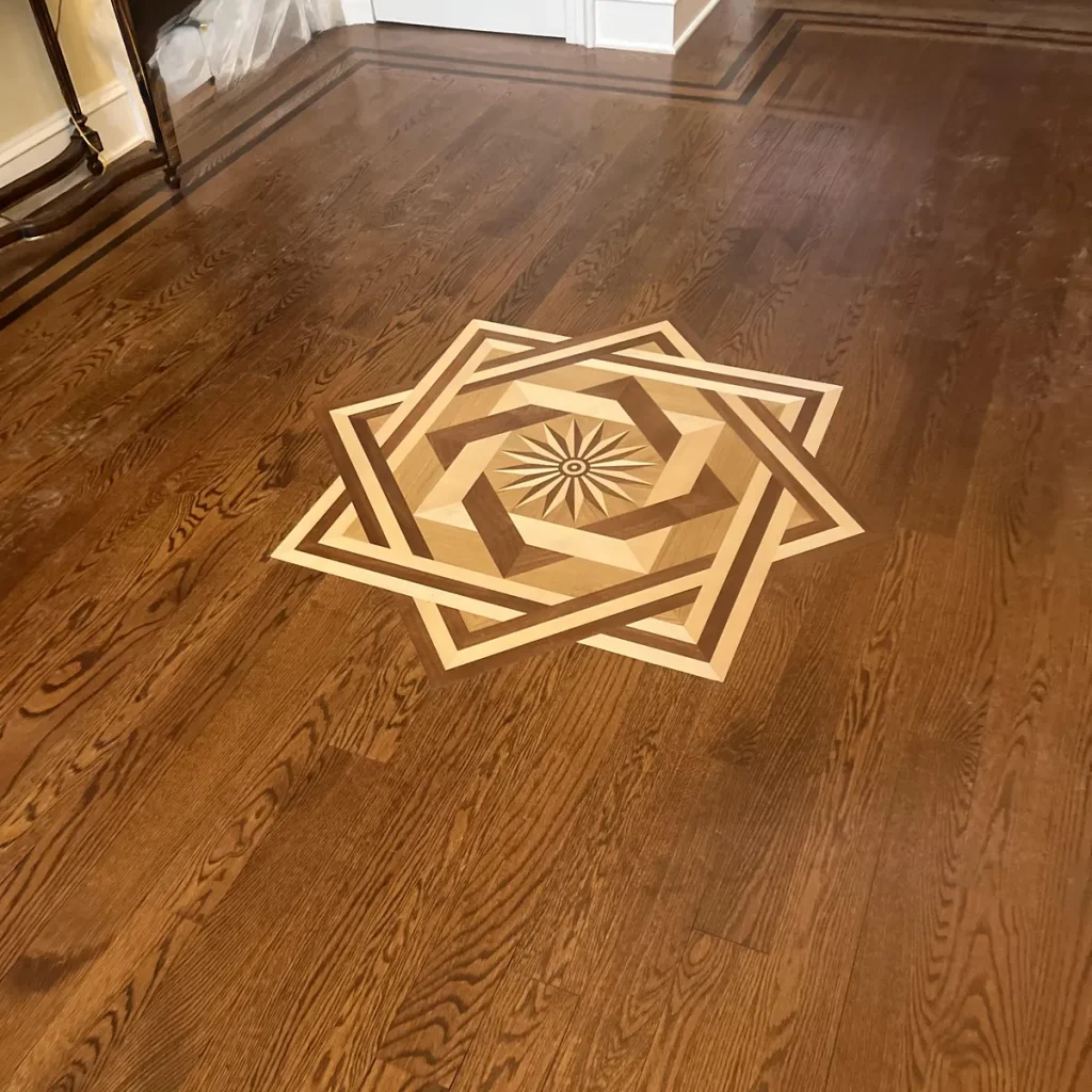Inlaid wood medallion, an eight-point star in light and dark woods with a sunburst center, set into an oak floor with a contrasting border