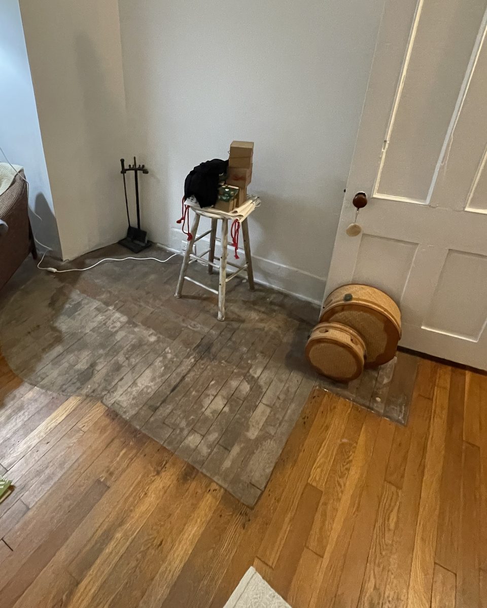 Gray, weathered floorboards in the outline of an old hearth, next to finished oak flooring
