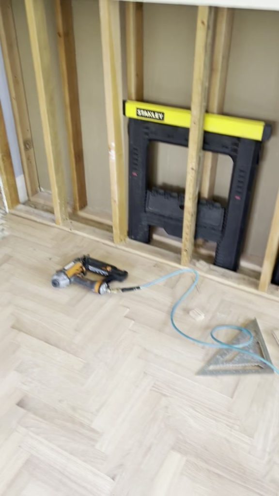 Herringbone wood floor being installed, with a nail gun and offcuts on the floor
