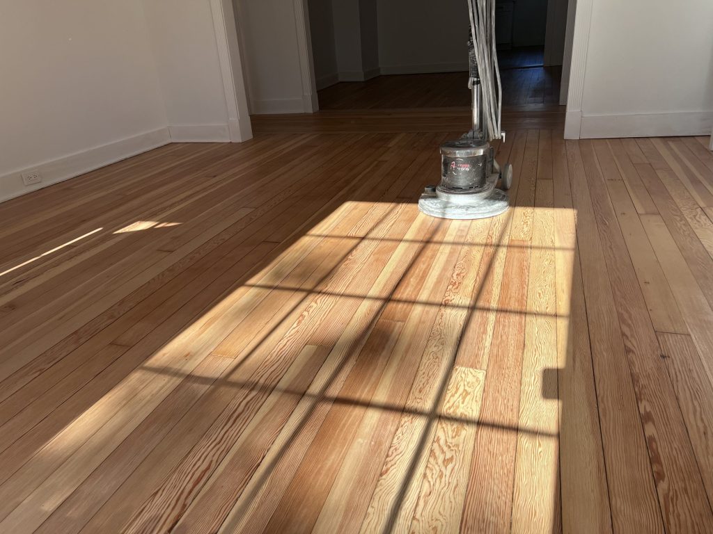 Freshly refinished wood floor in afternoon sun, with a floor buffer in the next room