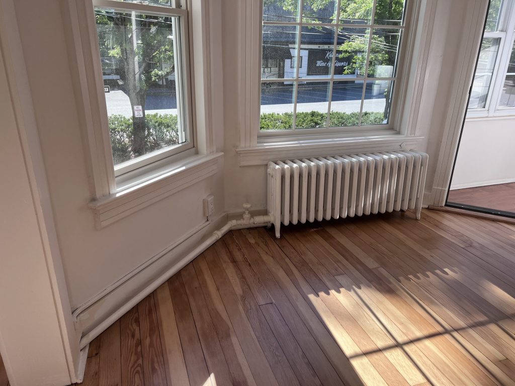 Sunlit corner of a refinished wood floor beside a window and radiator
